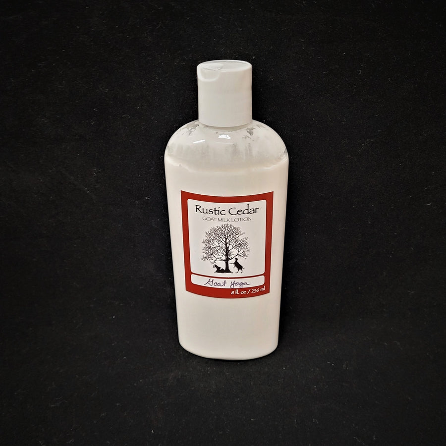 Single bottle of Rustic Cedar Goat Milk Lotion standing straight up. White liquid can be seen through clear plastic around the rectangular label in the center. The label has a rust-colored border with the black tree and goat logo in the center. Above the logo is the text Rustic Cedar Goat Milk Lotion and below in script Goat Yoga with 8 fl.oz. /236 ml below that.