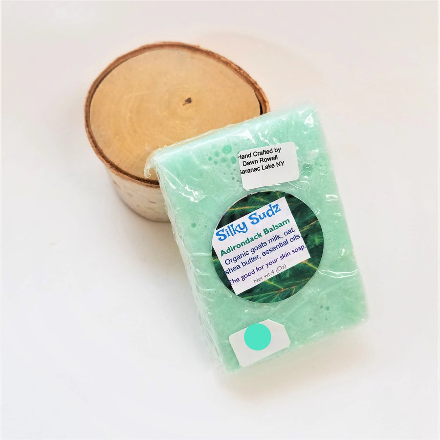 Sea green bar of Adirondack Balsam Silky Sudz soap leaning on a small birch round.