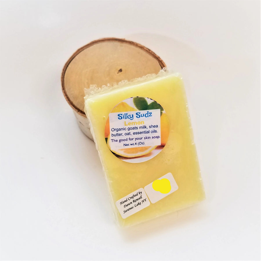 Yellow bar of Lemon Silky Sudz soap leaning on a small birch round.