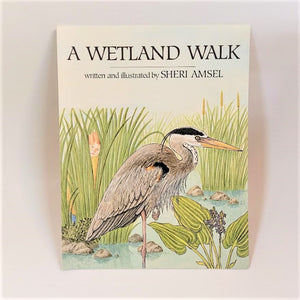 Cover of A Wetland Walk. Author Sheri Amsel illustration on the lower two thirds of the cover with child's head peeking through tall marsh grass at a heron. Black type above the illustration ona white background.