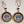 Dangling Winter Carnival circular earrings. Gold braided bands and black band surround Saranac Lake Winter Carnival blue, white & black logo.