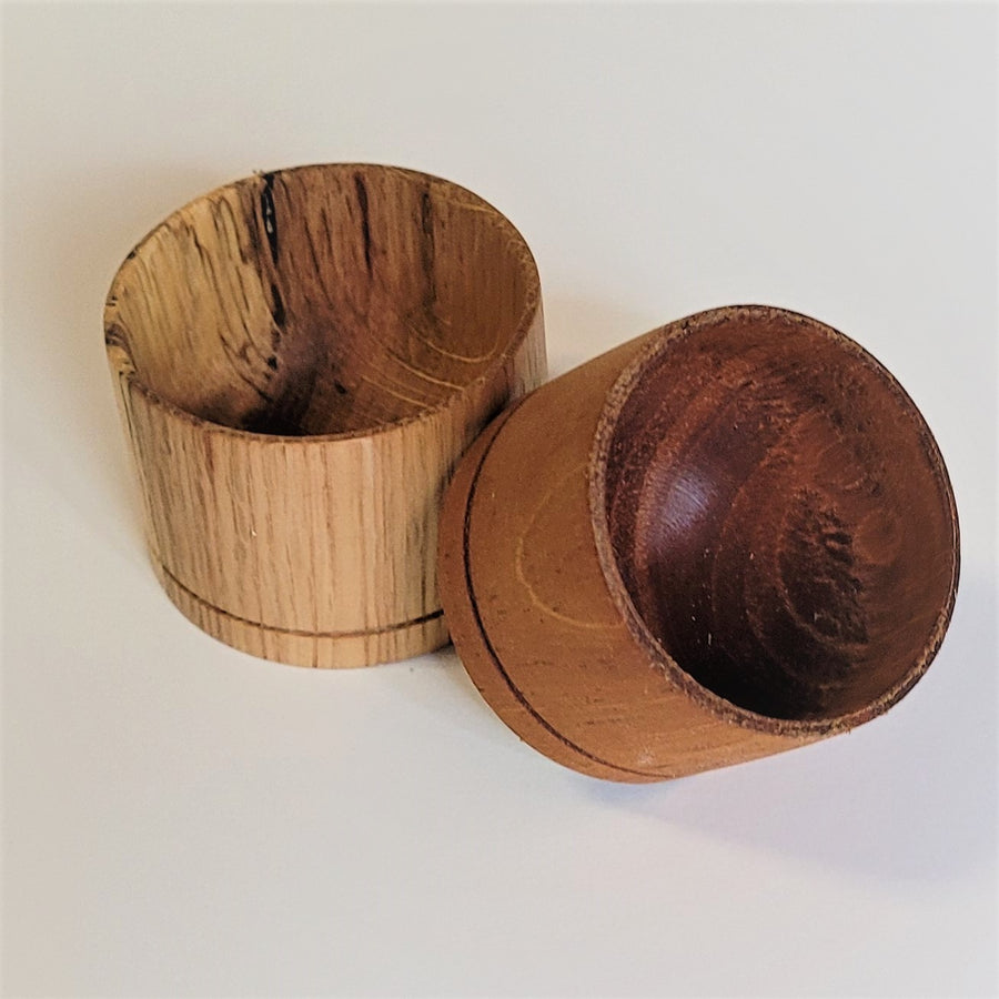 Two end grain bowls on a white background. The one of the left is a lighter wood and stands upright. The one on the right is a darker, redder wood and is tilted on its side.