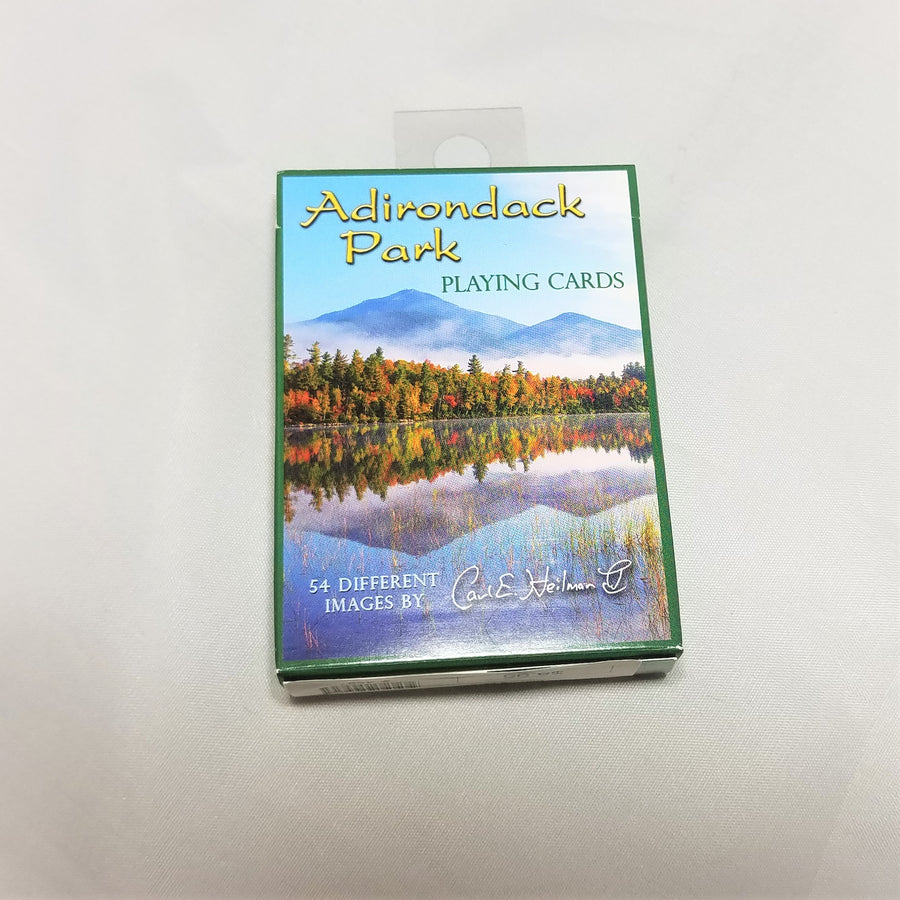 cover of boxed playing cards featuring green lettering on a blue sky atop white crested mountains, golden, green vegetation all reflected in the silver gray water.