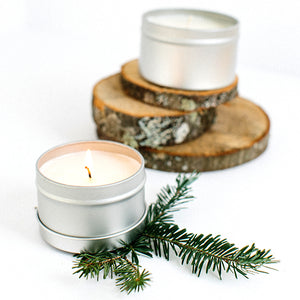 Top to bottom--silver candle tin atop 3 pieces of birch; open candle tin with lit candle atop a sprig of evergreen