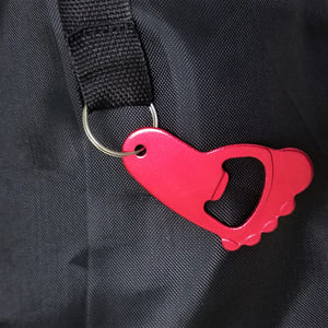 Red metal bottle opener, shaped like a paw, attached to a black strap hanging from the black carrying case.