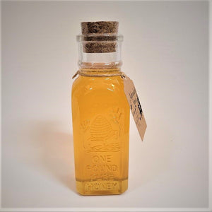 Single glass bottle of one pound size Adirondack Honey. Cork stopper top. Cord around the neck with the Adirondack Honey label hanging on the right.