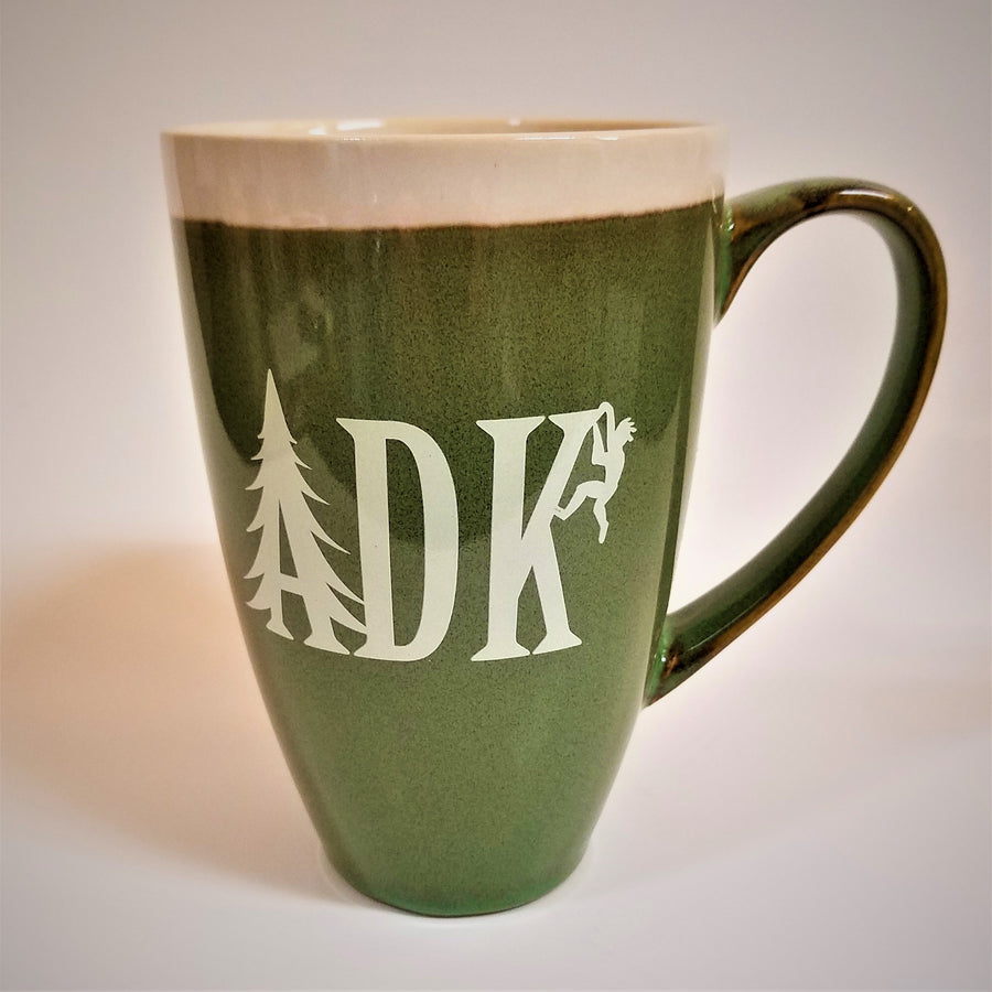 Tall green mug with whie stripe around the top with white imprint featuring the letters ADK with the A in the style of a pine tree and a small hiker climbing the top of the K.  Extra large handle visible on the right side.