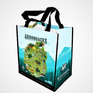 Full view of Adirondack map shopping tote. Black handles on top of a  bag in various shades of aqua and green with the word ADIRONDACKS in uppercase across the top .  The iconic green map of the Adirondack Park is in the center of mountains and trees. A directional icon and two bears rest on opposite sides on the bottom front. The side panel features mountains and forest and  white lettering: ADK BE OUTDOORS Leave It Better