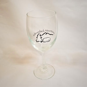 Clear wine glass with black text and black illustration of a bear, pine tree, and mountain outline.