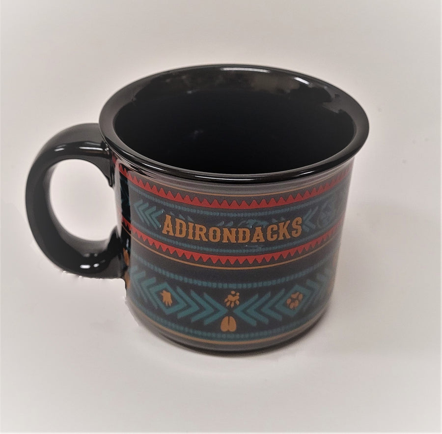 Black ceramic mug with solid black handle (left) and solid black interior. Pattern showing front has letters ADIRONDACKS in burnt sienna with a pattern of blue and red arrows designed with burnt sienna lines and paw prints in the bottom segment of the design.