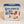 Blue and white box stands upright with Balance the Baker in blue typo next to and above a photo of the rounded baker holding tiny wooden pies and plates surrounded and 3 sets of wooden baked goods positioned around round baker bottom.