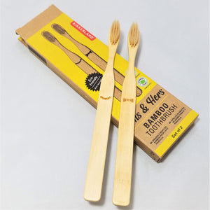 Two bamboo toothbrushes (hers on left with 5 beads below bristles; his on right with bow tie below bristles) set on top of the box package that they come in.