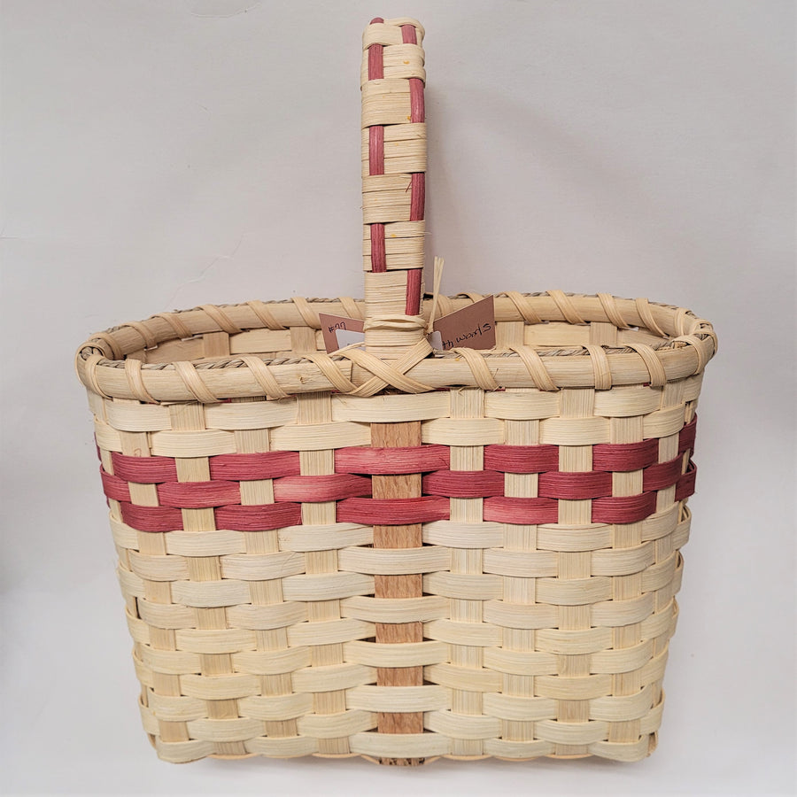 Woven wine basket in neutral color with mauve trim in top third of basket and mixed in with handle above the basket.