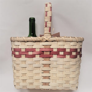 Woven wine basket in neutral color with mauve trim in top third of basket and mixed in with handle above the basket. The top of a green wine bottle can be seen on the left side.