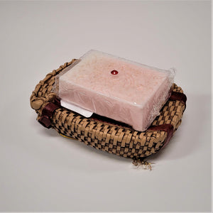 Pack basket soap dish with a bar of pale pink soap in plastic wrap sitting on top. 