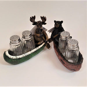 Moose in green canoe with clear glass salt and pepper shakers on the left and bear in red canoe with clear salt and pepper shakers on the right.