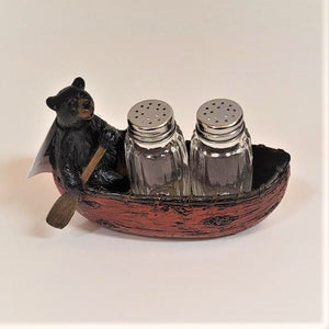Bear with brown paddle on left side of red canoe holding clear glass salt and pepper shakers.