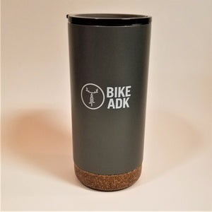 Charcoal tumbler with cork-like bottom stands upright with the text BIKE ADK in white lettering and the iconic bicycle with antler handlebars in a white circle next to the type. A thin black lid is visible at the top of the tumbler.