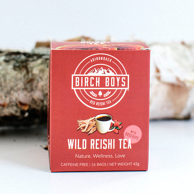 Red box of Birch Boys Wild Reishi Tea standing upright in front of a birch log. 