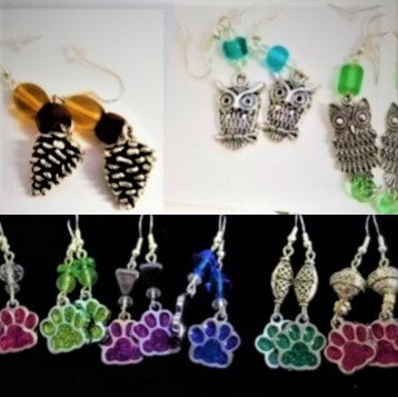 Top left  to right: silver pine cone earrings with gold and brown glass beads above; two pairs of silver owl earrings--one on left has aqua-blue glass beads above the owls, on right green glass beads above and below the owl. Below are dog paw glass earrings in pin, green, purple, blue, dark green, red (left to right).