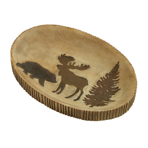 Beige-colored oval soap dish with brown accents and images. What look like mini brown logs edge the oval-shaped dish while a bear, a moose and an evergreen appear on the surface of the soap dish.