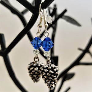 Silver pine cone earrings hanging from black earring tree. Clear glass and blue glass above the earrings on silver hangers.