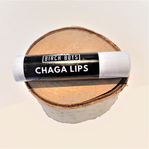 Closed tube of Chaga Lip Balm resting on a round birch block. The label is black with white lettering and each end is white.