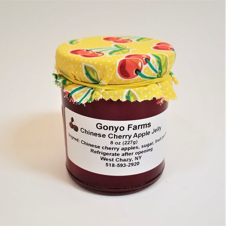 Colorful yellow cloth with red cherries banded to a jar of Gonyo Farms Chinese Cherry Apple Jelly.