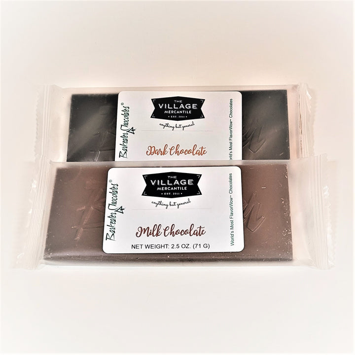Two chocolate bars with The Village Mercantile Label centered on clear plastic wrapping so the bar can be scene around the label. Top is dark chocolate; bottom milk chocolate