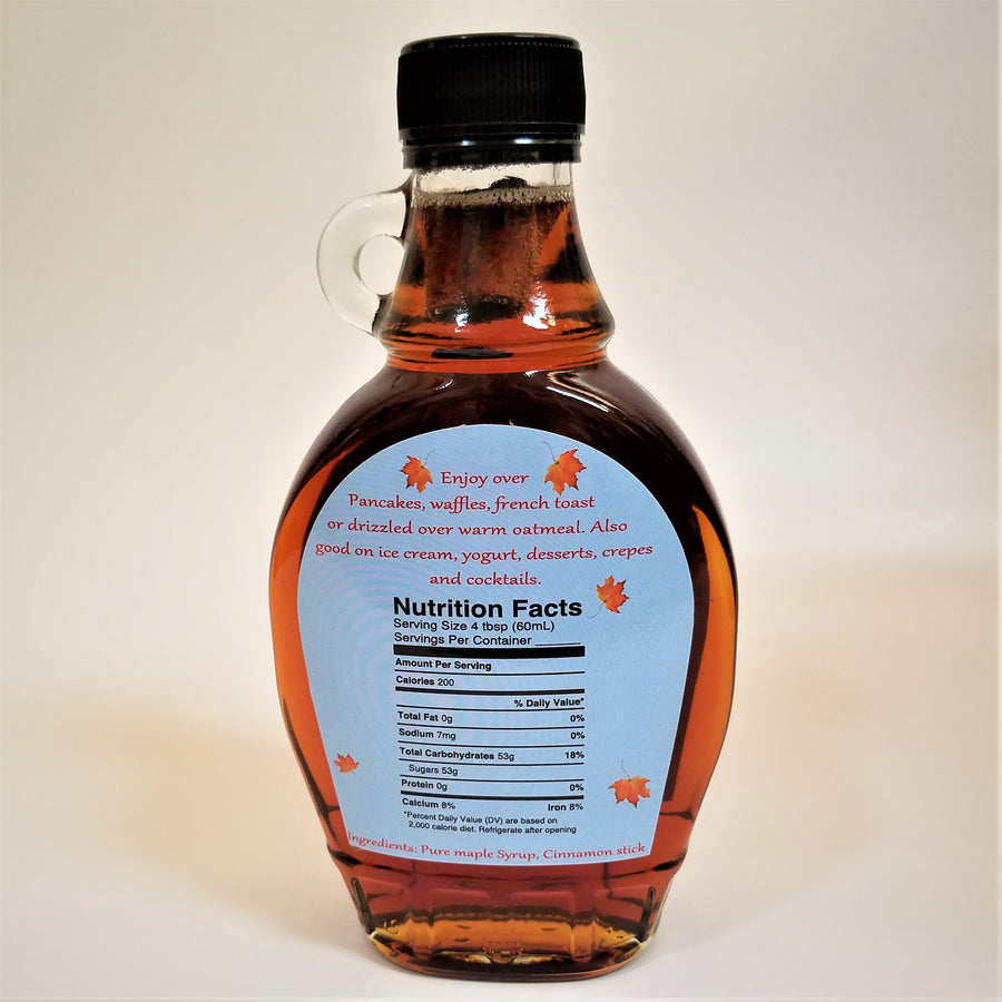 Upright clear maple syrup bottle  seen from the back. The small clear glass handle on the left side. Black screw cap on top,  back label on 2/3 of the bottle includes Nutrition Facts