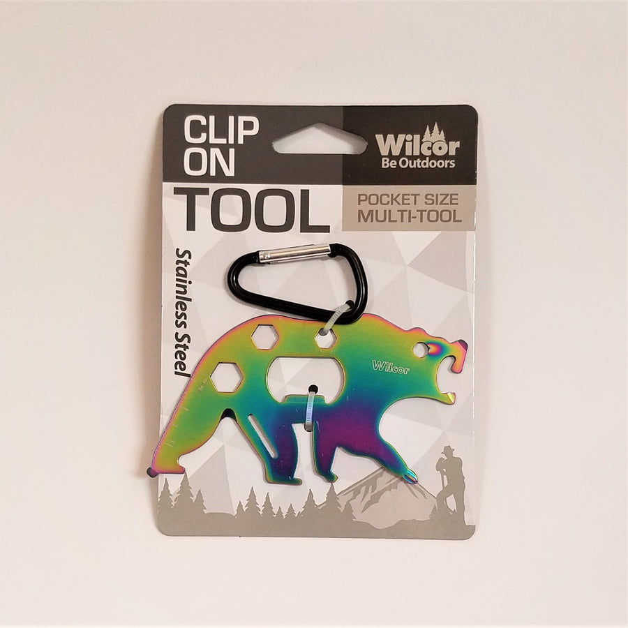 Clip-on Bear Tool in packaging. Stainless steel bear appears with a purply blue bottom and shades of green for upper body and mouth.ter and blue edge. Black and silver carabiner clip is fastened above the bear's back..