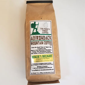 Brown-bag package of Hiker's Delight Adirondack Mountain Coffee. White label placed vertically in the center with green, brown and black type. Green illustration of a hiker and black outline of the Adirondack Park on top of label.