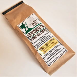 Brown-bag package of Midnight Moon Adirondack Mountain Coffee laying on a white background. White label placed vertically in the center with green, brown and black type. Green illustration of a hiker and black outline of the Adirondack Park on top of label.