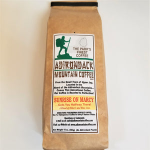 Brown-bag package of  Sunrise on Marcy of Adirondack Mountain Coffee. White label placed vertically in the center with green, brown and black type. Green illustration of a hiker and black outline of the Adirondack Park on top of label.