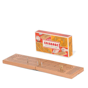 Cribbage game box standing upright behind the flat cirbbage board with six pegs placed standing on the board.