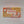 Rectangular box of Cribbage game left top corner illsutrates playing cards in a hand and in two piles with part of a cribbage board, right top corner part of the cirbbage board on a mustard background, left bottom another part of the board on the mustard backgroung, right bottom cribbage board flat with a hand over it and two cards face up next to it.