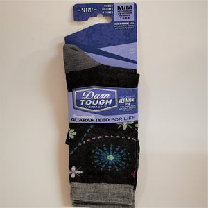 Full view of Darn Tough socks in their blue and white labeled packaging.  Women's solid black with blue, white, pale green, pale lilac flowers and dotted lines, gray heel, gray cuff