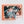 Box cover for Decidedly Different Saranac Lake jigsaw puzzle. Box border is rectangular orange around pieces in shades of blue, green, red, yellow with black borders.