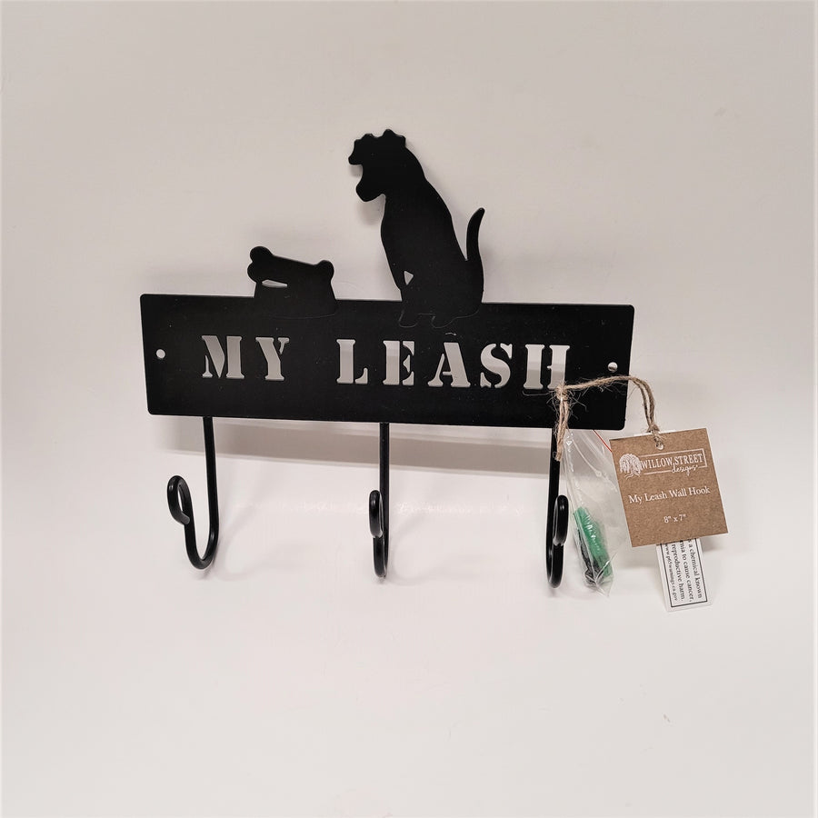 Black metal 3-hook leach rack with etched out letters MY LEASH above the hooks and black metal cut-out of dog and dish and bone above the rack. plastic package attached with screw accessories and brown tag to the right.