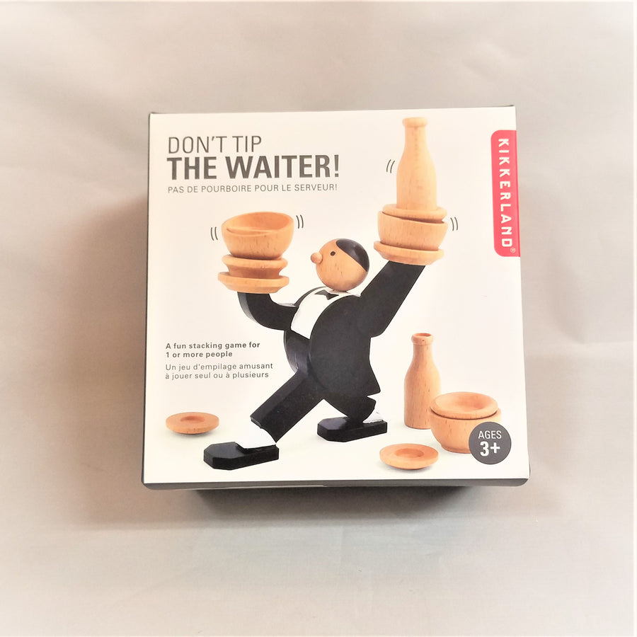 The front of the Don't Tips the Waiter box with a picture of the wooden set ...waiter dressed in painted black-and-white tux-like attire holding up small wooden bowls dishes and decanters. At his feet are more wooden dishes, bowls and a decanter.