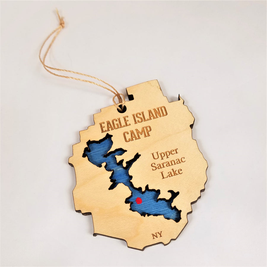 Eagle Island ornaments with twine hanger above. Cream-colored with EAGLE ISLAND CAMP lettering on the top, and a blue lake cut out with a red dot for Eagle Island.  Upper Saranac Lake lettering on the right.  NY letters on the bottom.