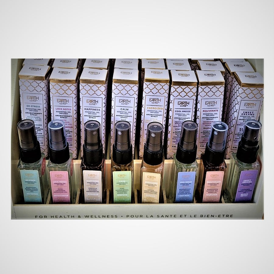 Eight glass bottles of different Earth Luxe aroma therapy scents stand upright in a display with their boxed counterparts standing upright behind them.