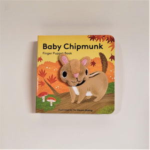 Baby Chipmunk finger puppet book with cloth head of chipmunk coming out of the flat book cover. Chipmunk is beige with black and white stripes and a brown tail. Drawn on a brown path with mushrooms and bushes surrounding.
