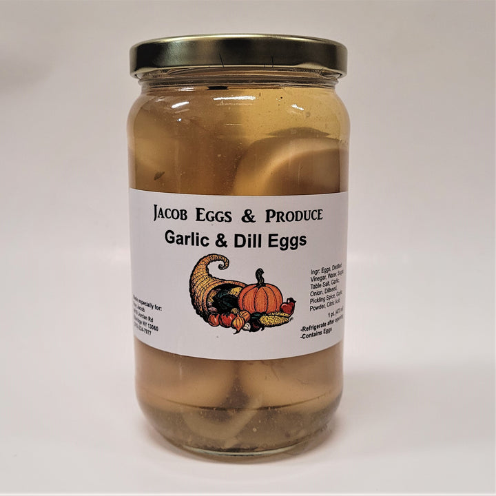 Jar of Jacob Eggs & Produce Garlic & Dill Eggs. That text is featured on a white label that encircles the middle of the jar. There is a cornucopia with colorful gourds below and between the black text. The jar has a gold twist lid and some of the eggs and seasonings can be seen through the glass jar.