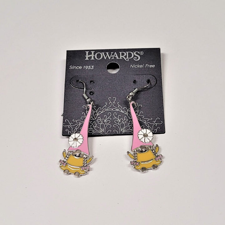 Playful-looking gnomes hang from silver hoops on black Howard's packaging. The gnomes each have long pink pointy hats with a white flower near the bottom on the outside edge. The body of the gnome is gold with a silver nose and two braids hanging from the hat on each side of the nose.