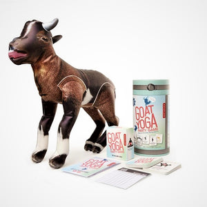 Cylindrical Goat Yoga container stands upright with the contents displayed. A Goat Yoga Party Game box, cards, 2 items lying flat with Goat Yoga logo on top and one scoring pad. Overshadowing all of this on the left is the inflated brown and white horned goat.
