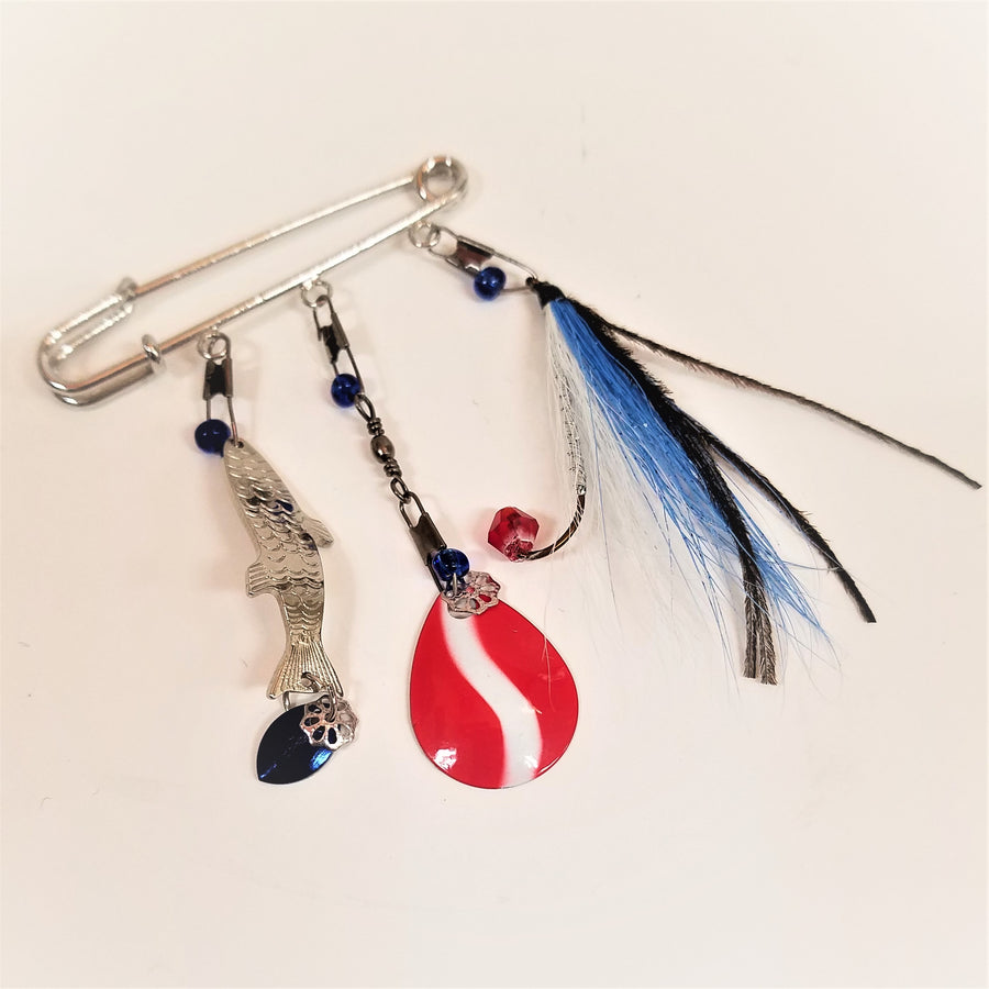 Allurement hatpin by itself on a white background. Hanging from the pin are a silver fish lure, a red and white spinner, and blue, black an white lure.