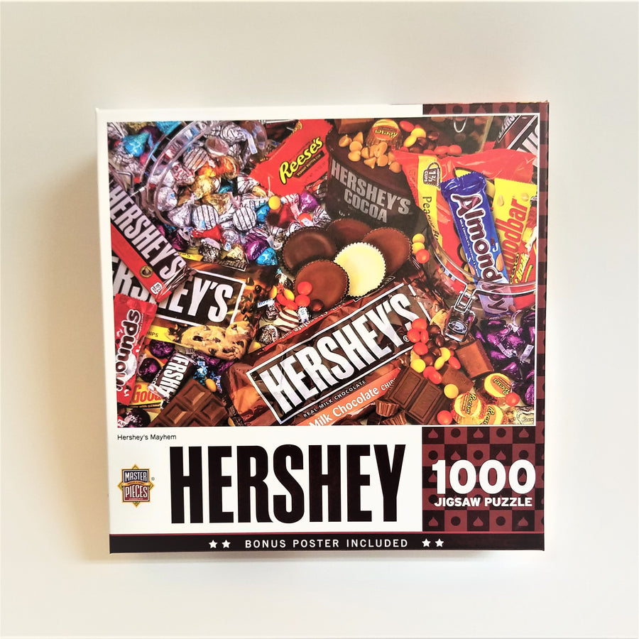 Cover of Hershey 1000 piece jigsaw puzzle. Full-color photo of various Hershey's chocolate products: Cocoa, Almond Joy, Mr. Goodbar, Resses, to name a few over a bottom border with text.