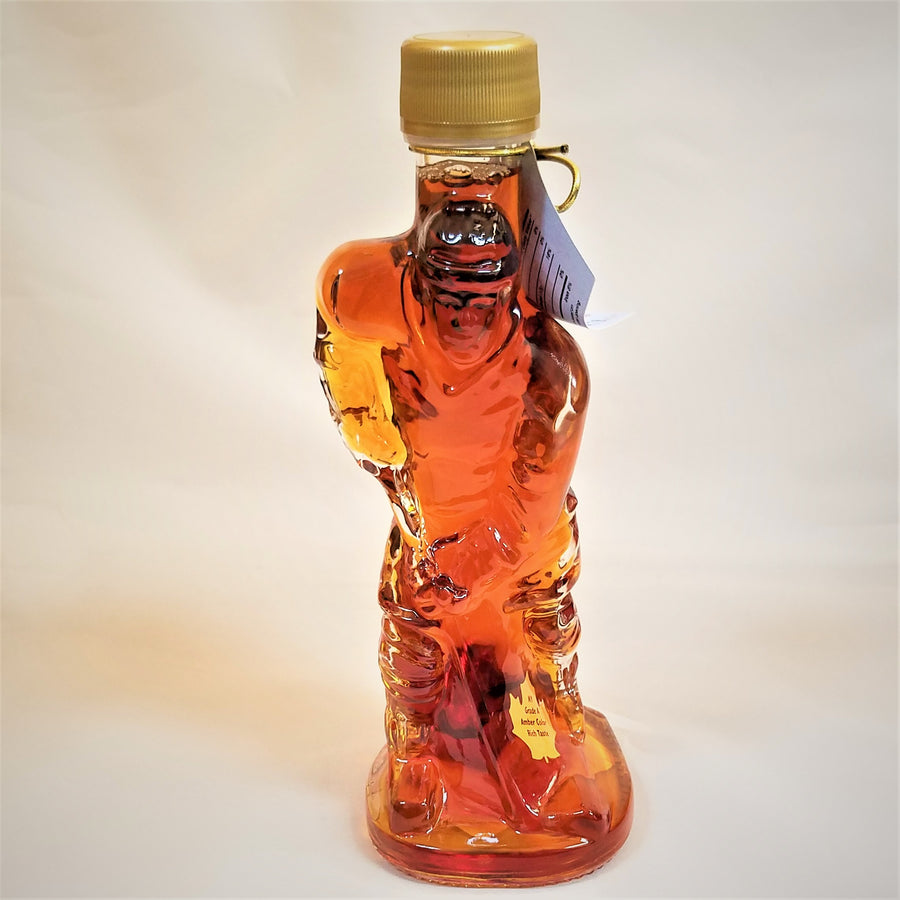 Glass maple syrup bottle filled with syrup and shaped like a hockey player with a gold-colored screw top on an off-white background.