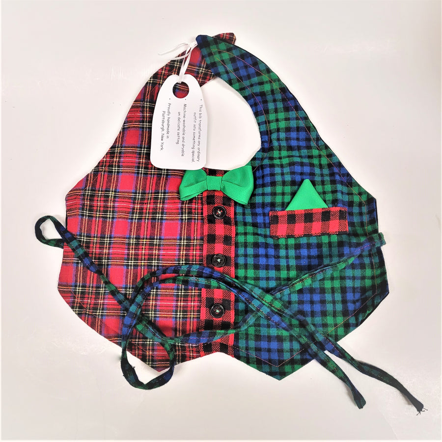 Plaid bib (left side red dominant pattern, right side blue and green with a red plaid pocket and green handkerchief triangle popping out. Green bow tie in center with 3 black buttons in a vertical line at the center. Two long blue/green/black plaid tie straps are arranged on the front. clasped at the back (neck).